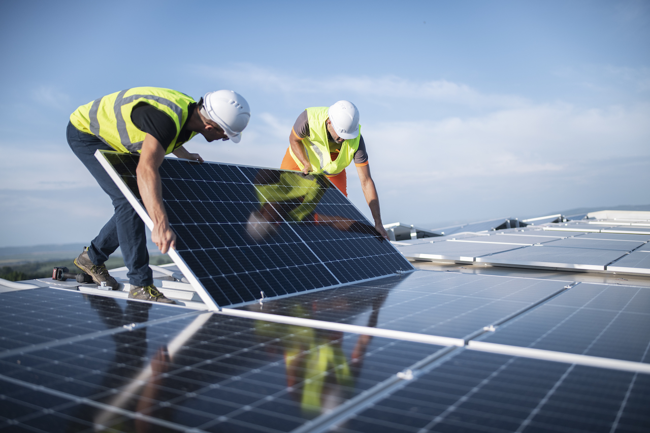 Two men install a solar panel on a roof; GettyImages-1405880267