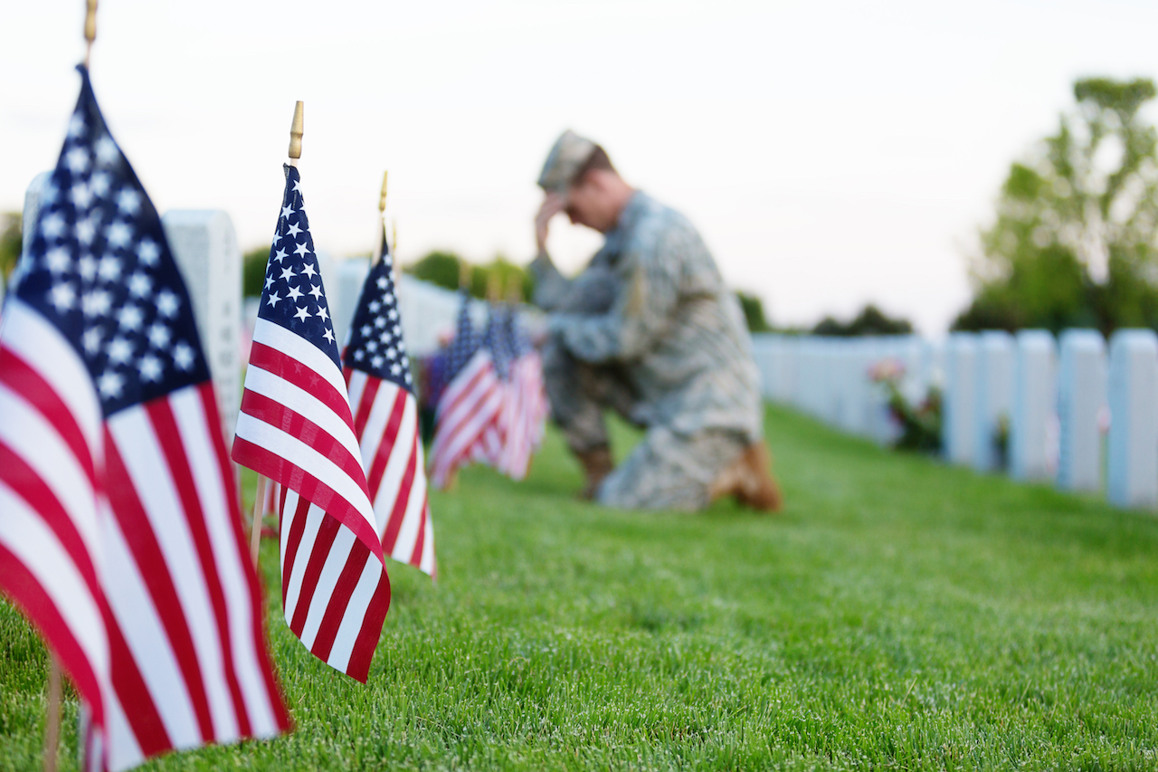 Soldiers kneels in front of flag-lined tombstones