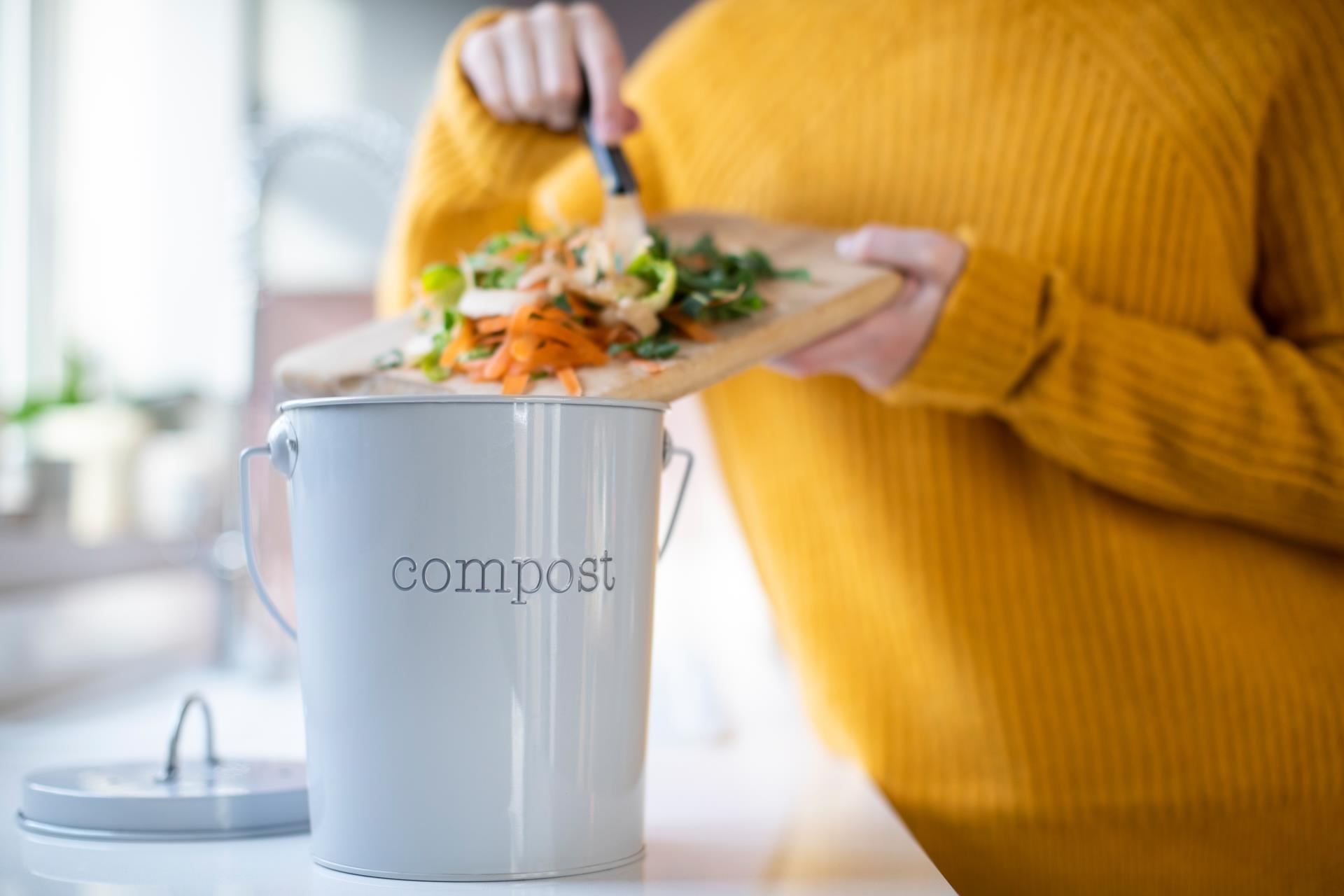 person putting vegetable scraps into compost bucket