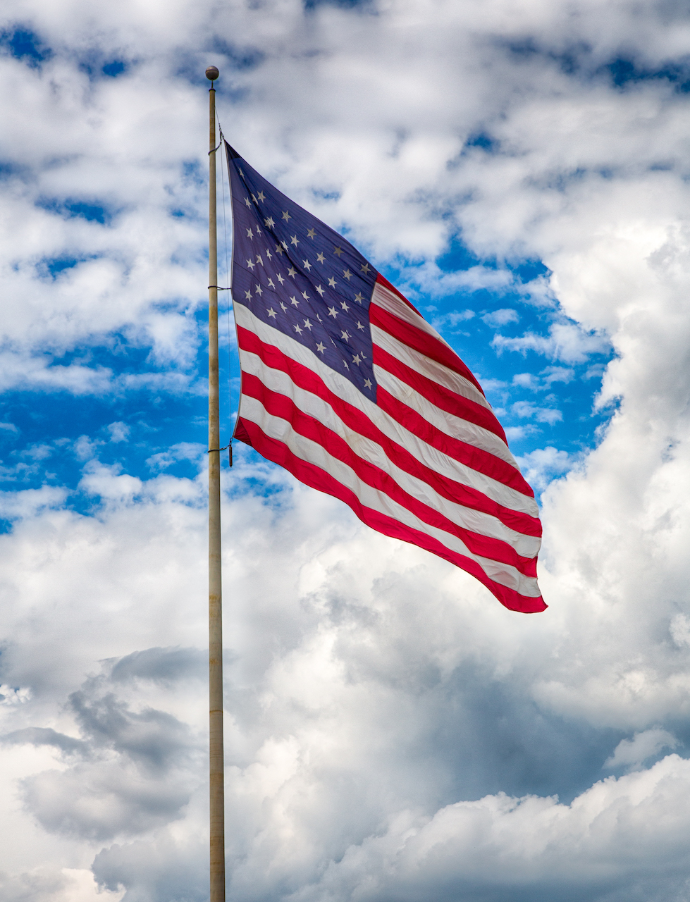 U.S. flag waves in front of a bright blue sky covered in puffy white clouds