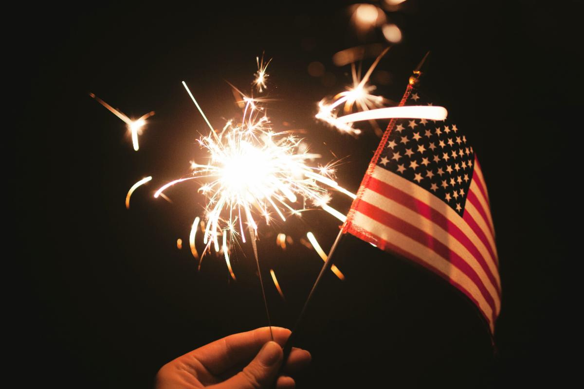 a mini flag and sparkler are held together on a dark background